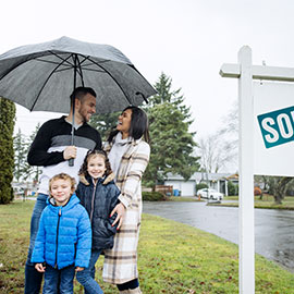 family standing under umbrella next to sold real estate sign
