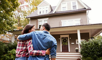 A couple with their arms around each other in front of a house.