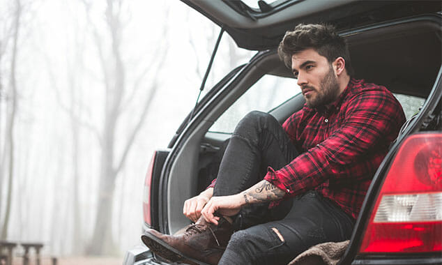 Man tying hiking boots while sitting in the back of an SUV