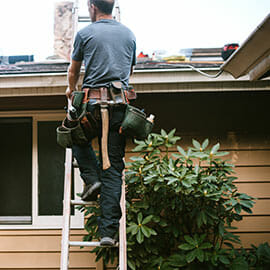 man on ladder repairing roof